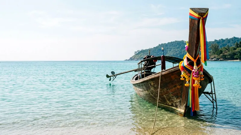 Ribbon-decorated longtail boat moored in clear turquoise shallow water on a Phuket beach.