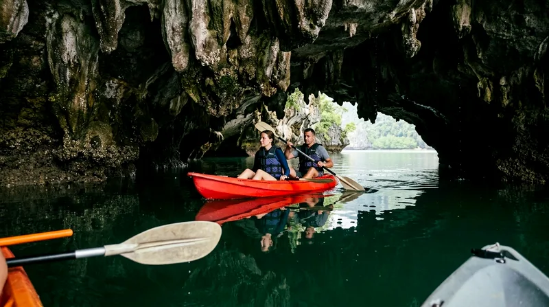 Kayak paddling through narrow cave beneath limestone overhang